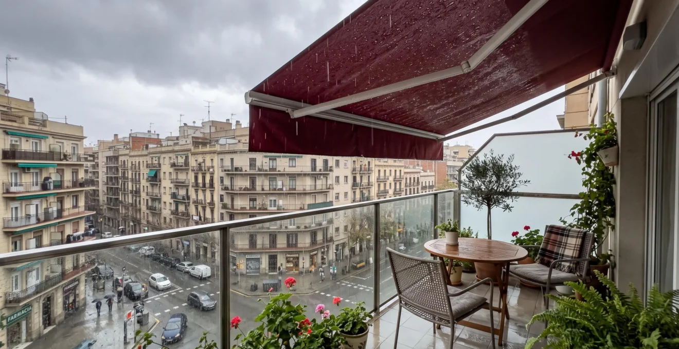 Balcón urbano español con toldo de guías desplegado protegiendo los muebles durante un día lluvioso de otoño