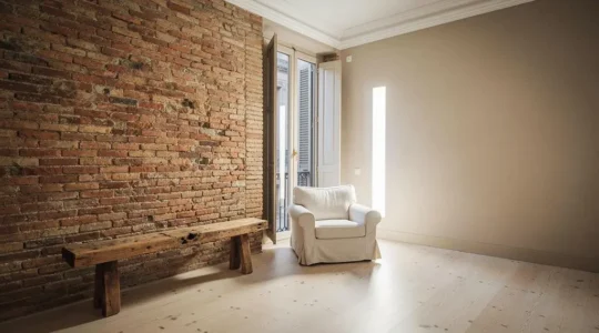 Salón de un piso español con una pared de ladrillo visto original junto a una pared lisa pintada, mostrando el contraste entre acabado natural y revestimiento tradicional.
