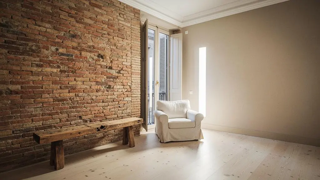 Salón de un piso español con una pared de ladrillo visto original junto a una pared lisa pintada, mostrando el contraste entre acabado natural y revestimiento tradicional.
