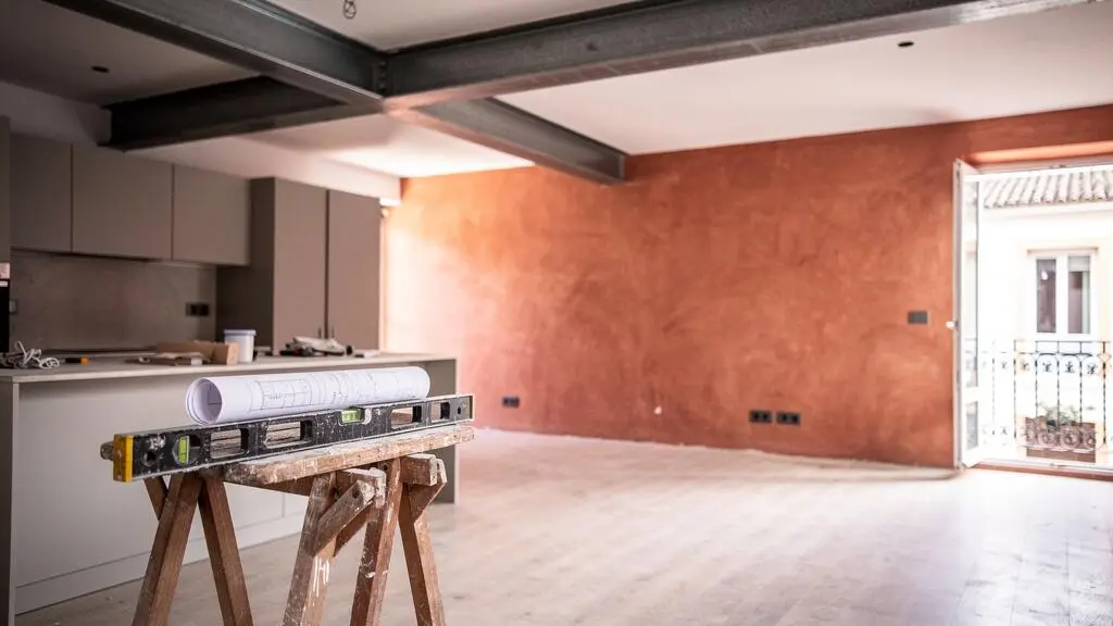Interior de vivienda española a medio reformar mostrando una viga estructural de acero integrada como elemento de diseño entre cocina y salón