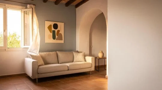 Salón luminoso de un piso español con una pared pintada en azul grisáceo que transmite frescor visual junto a una ventana con luz cálida de verano.