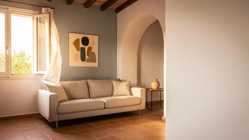 Salón luminoso de un piso español con una pared pintada en azul grisáceo que transmite frescor visual junto a una ventana con luz cálida de verano.